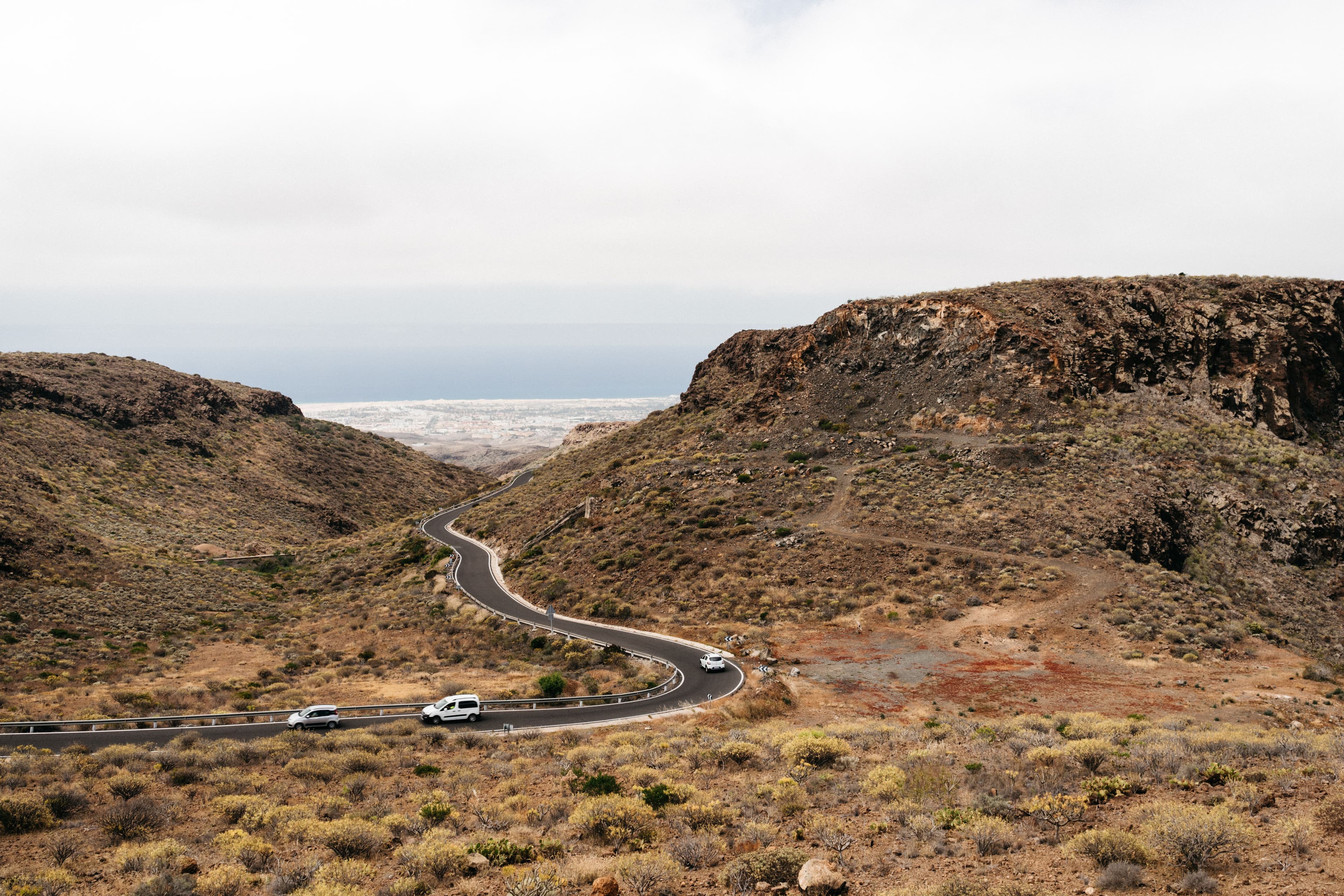 Cars descending an arid road toward Gran Canaria's coastal plain